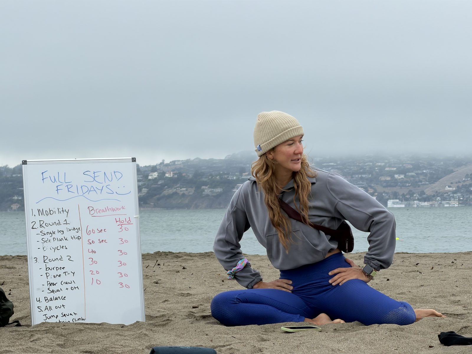 Dr. Emmy Haw beside the Full Send Fridays workout board at Ocean Beach